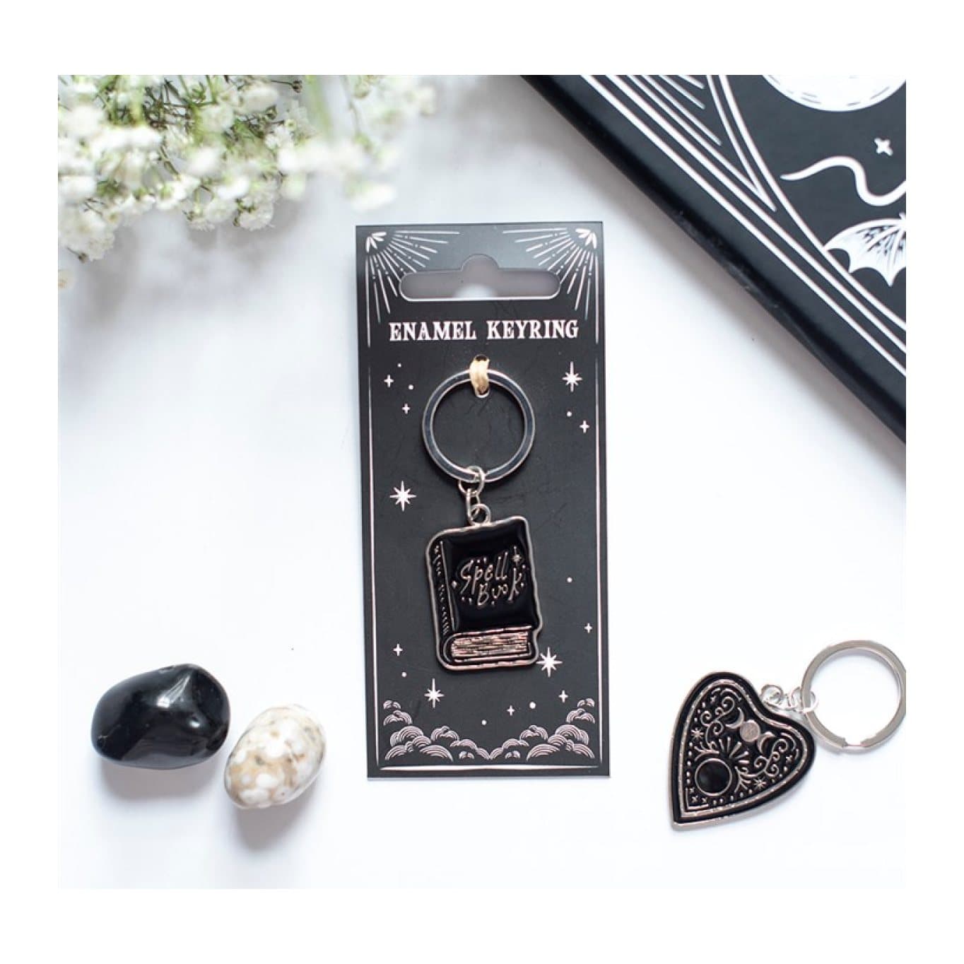 Black spell book keyring with enamel-style details on its cardboard back