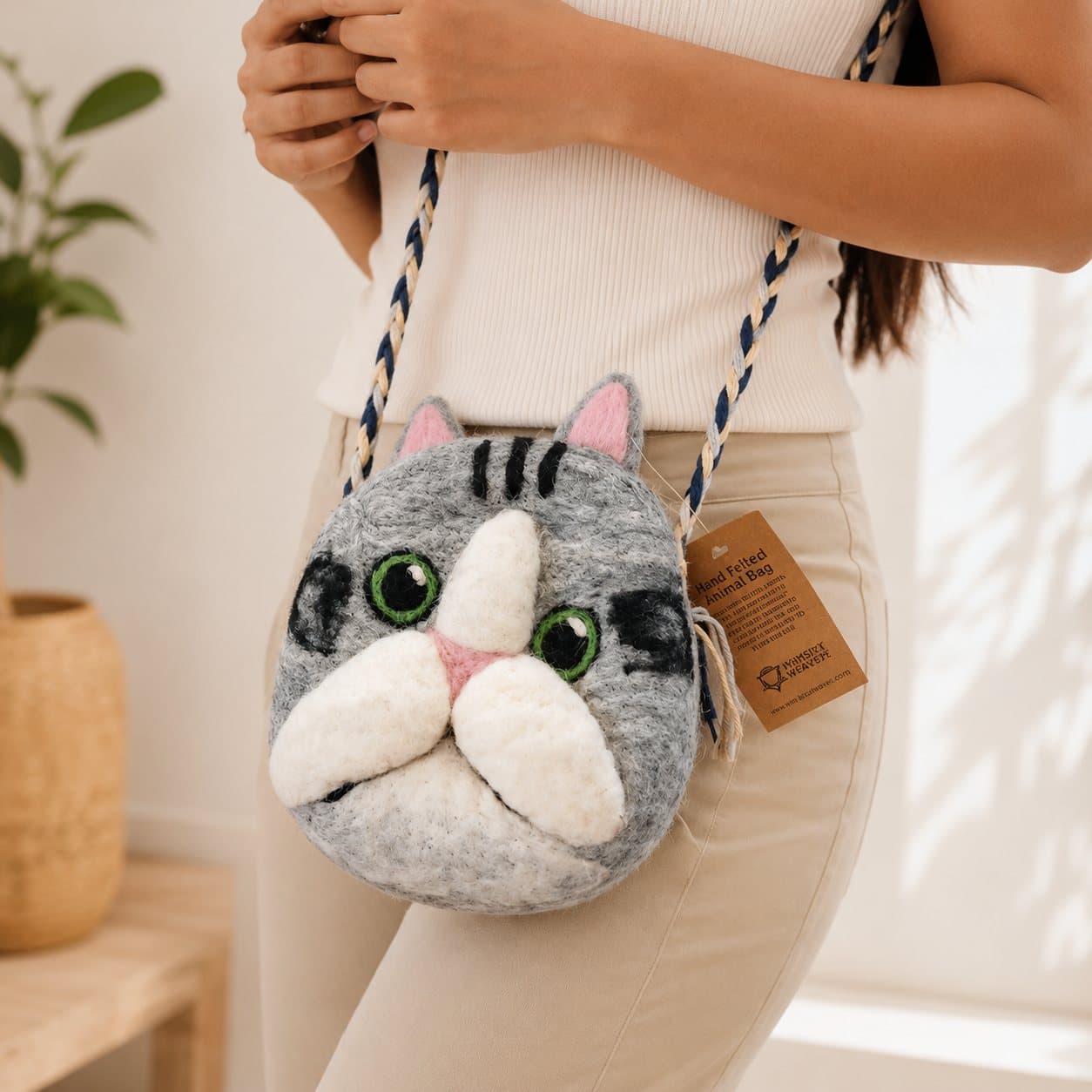Felted cat bag with bright green eyes, pink ears, white muzzle and a braided strap