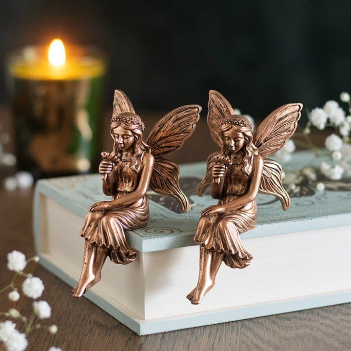 Two bronze fairy ornaments sitting on a shelf edge
