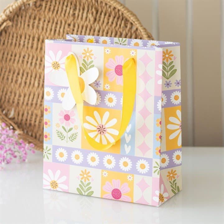 Floral patchwork print paper gift bag with yellow ribbon handles and daisy tag.