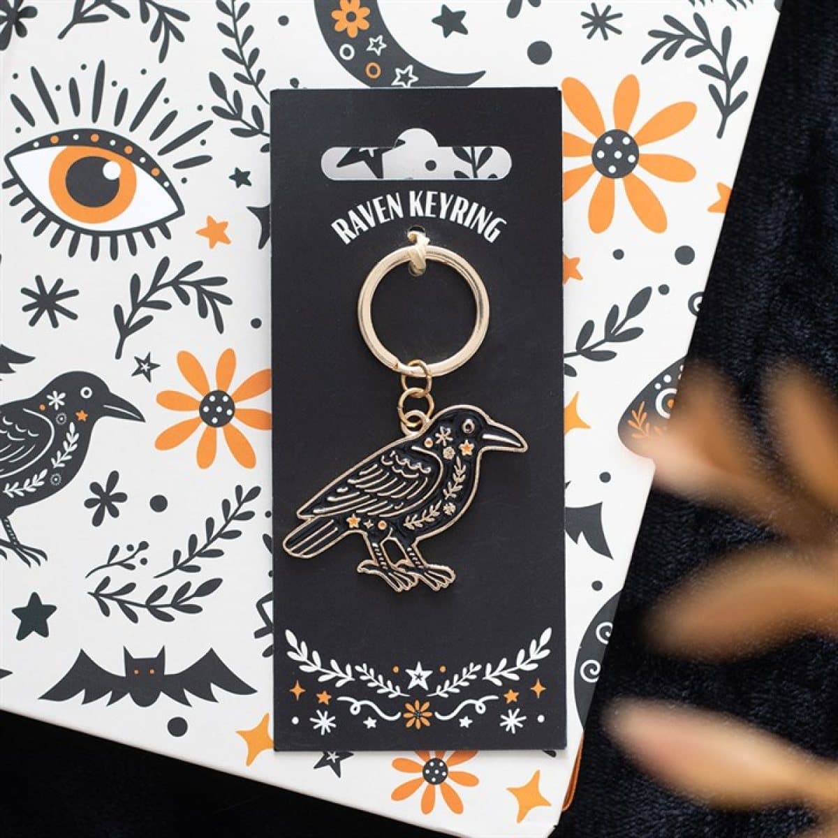 Folk raven keyring with a detailed enamel design on a cardboard back