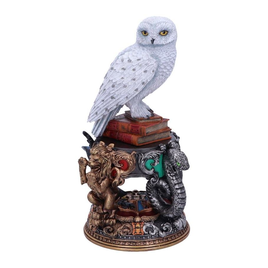 Hedwig owl figurine on a pile of spell books, with Hogwarts house emblems on the base