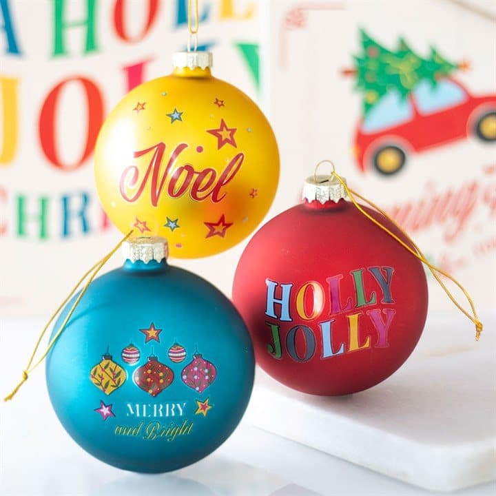 Three colourful glass Christmas baubles reading Holly Jolly, Noel and Merry and Bright