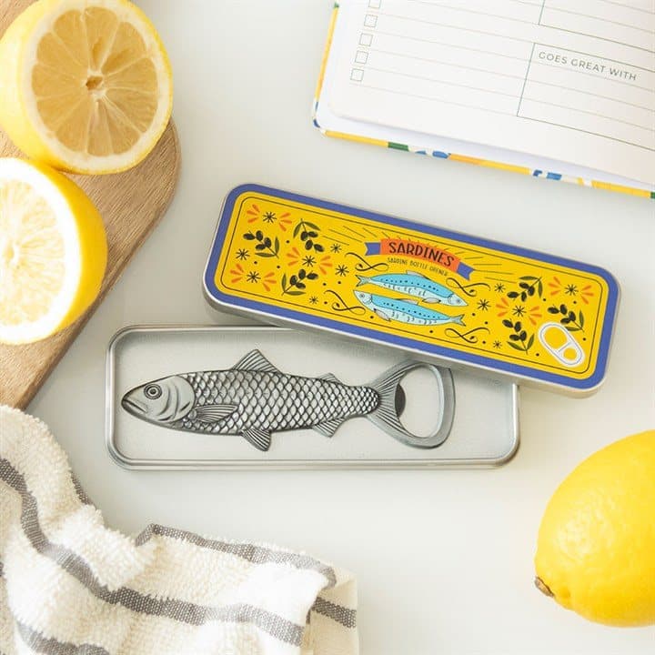 Fish-shaped metal bottle opener next to an open mini sardine tin