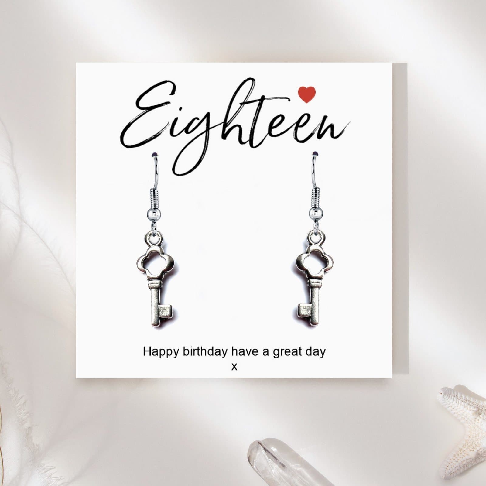 Silver drop earrings with key charms beside an 18th birthday message card
