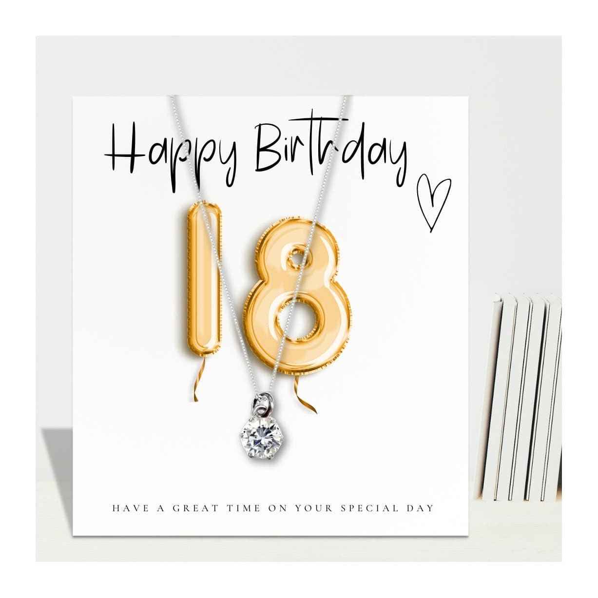 Sterling silver necklace with a cubic zirconia charm beside a gold balloons message card