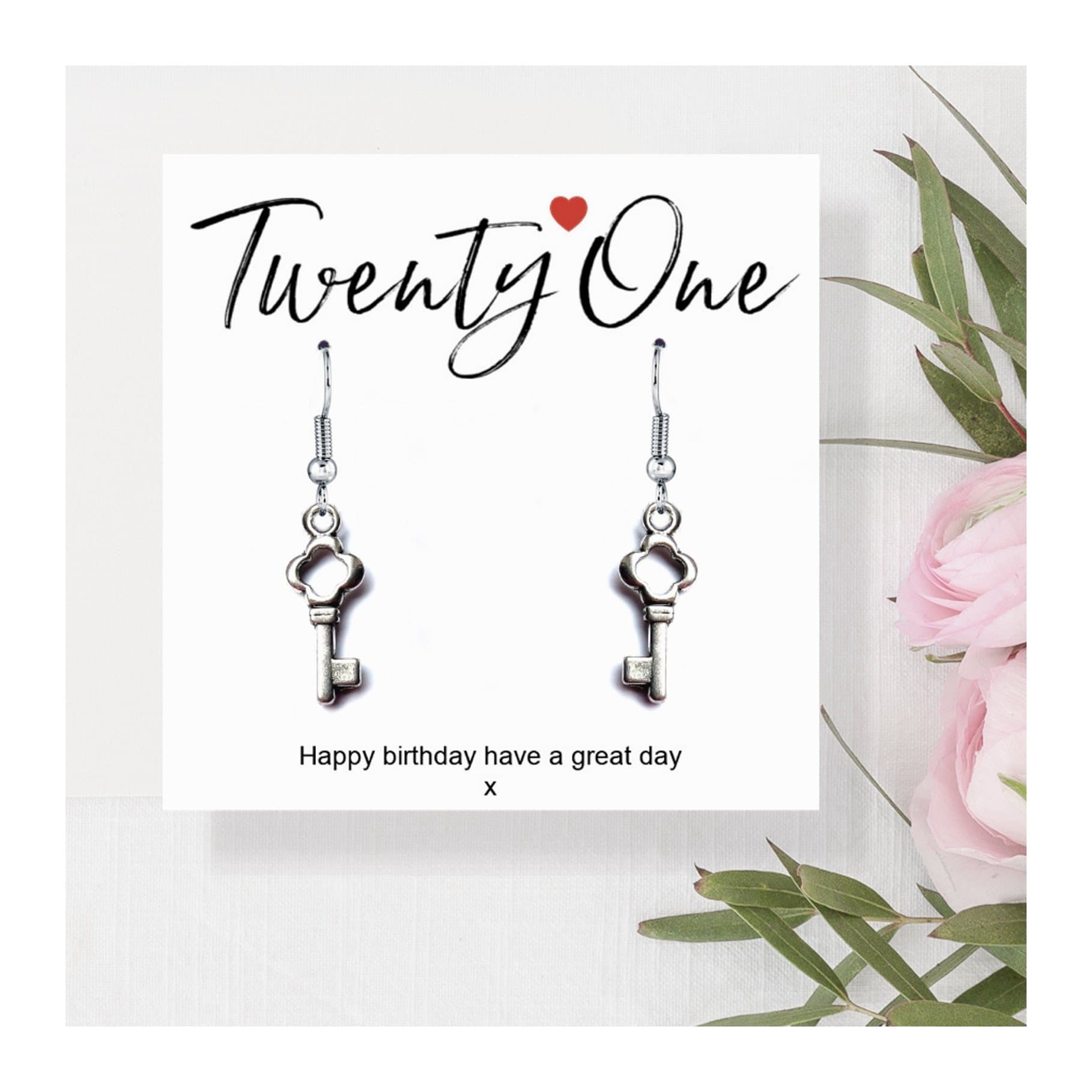 Silver drop earrings with a key charm beside a 21st birthday message card