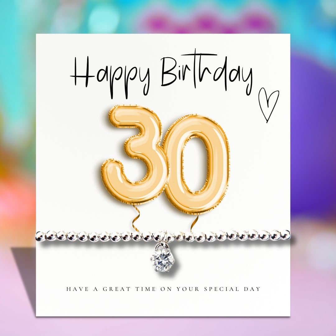 Silver stretch bracelet with a cubic zirconia charm beside a gold balloons birthday card