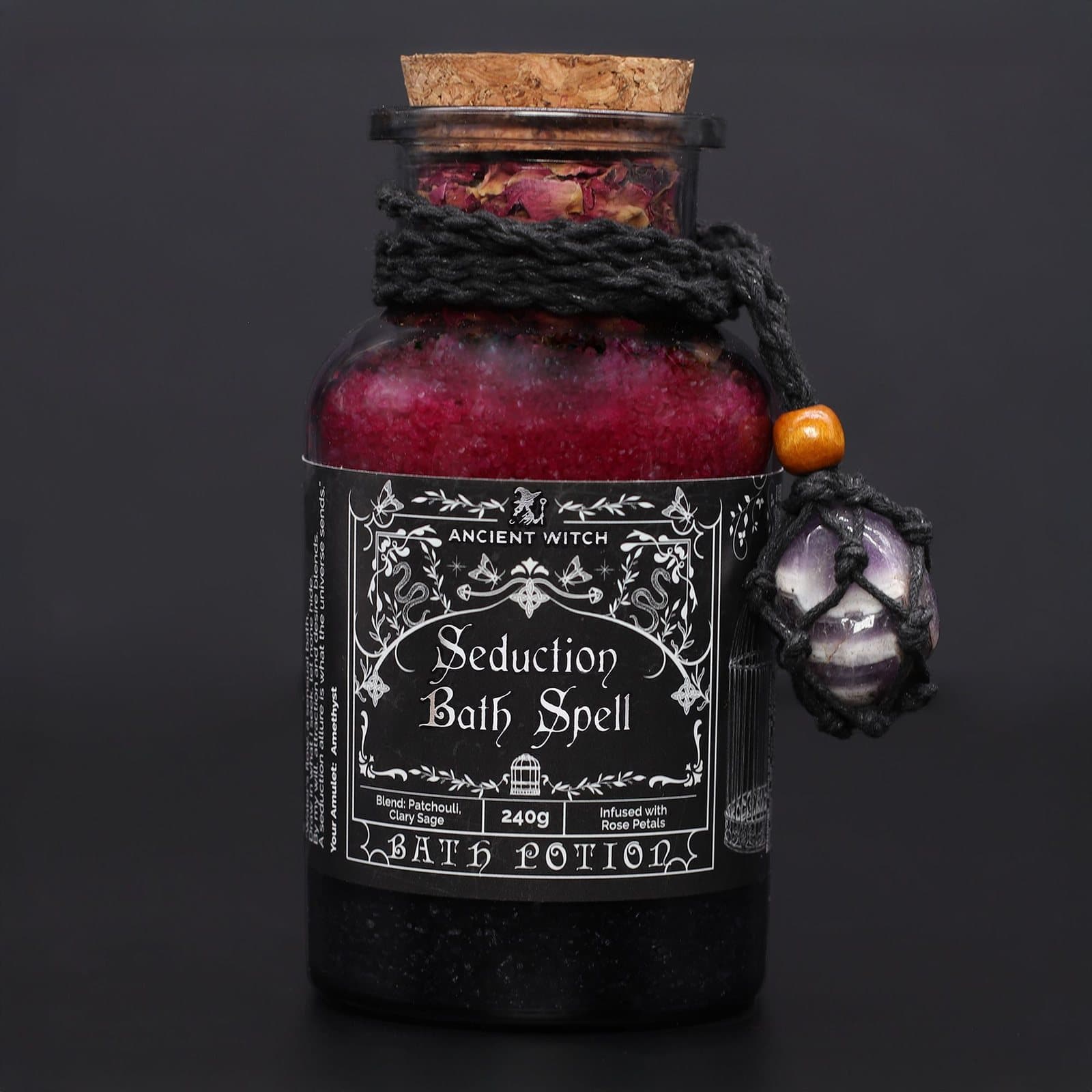 Apothecary-style glass jar of bath salts with dried rose petals and an amethyst amulet