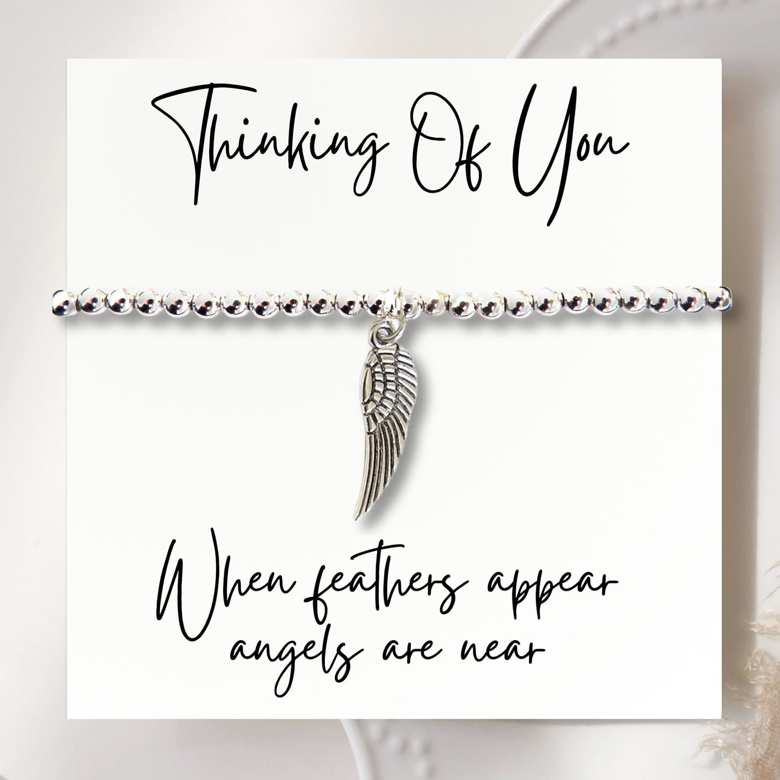 Silver beaded stretch bracelet with an angel wing charm beside a thinking-of-you card