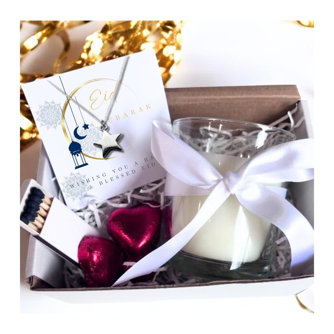Glass candle with an Eid Mubarak moon design, beside a silver star necklace.
