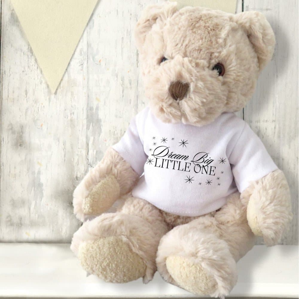 Teddy bear wearing a shirt printed Dream Big Little One in black writing with little stars