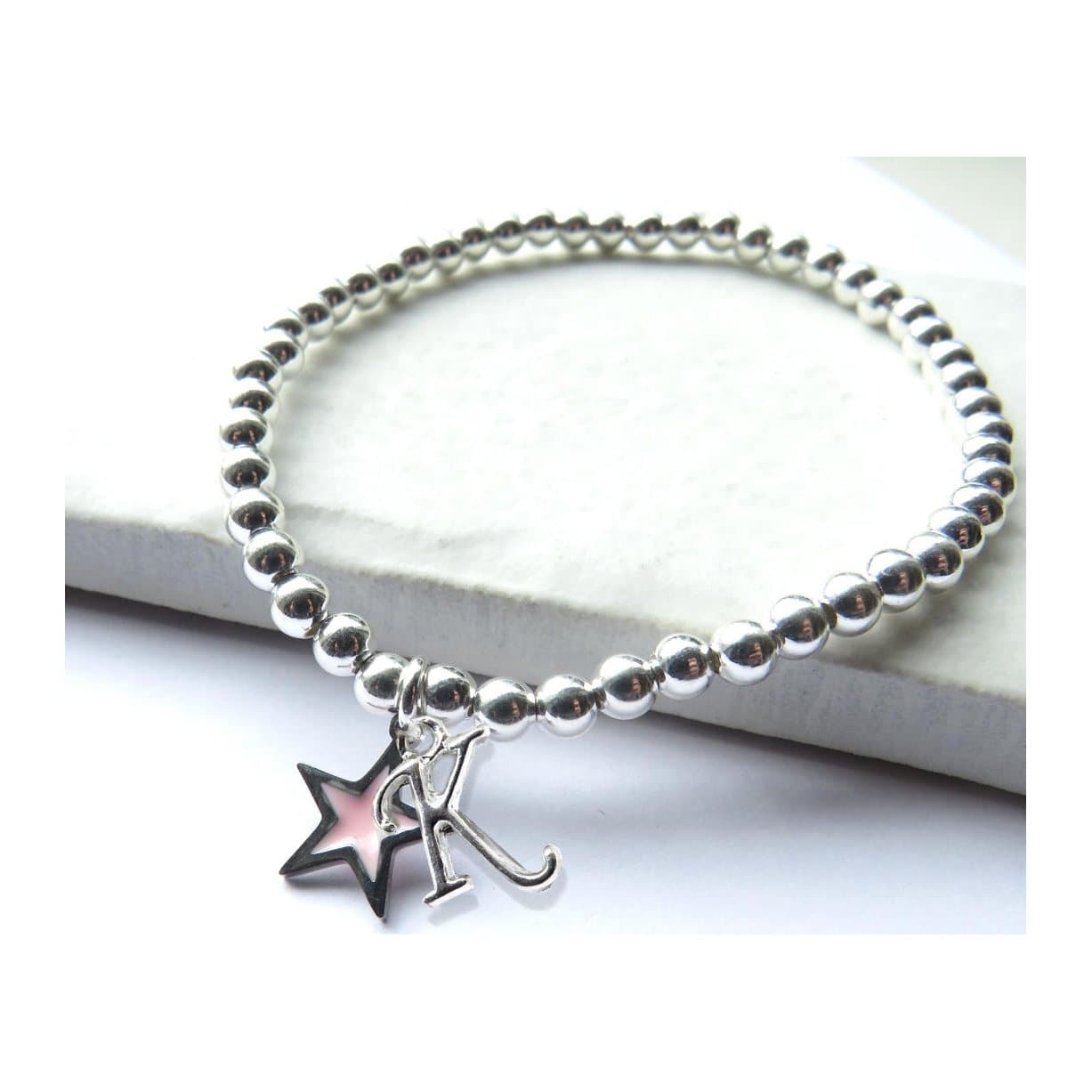 Silver beaded stretch bracelet with a silver initial charm and a pink enamel star charm.