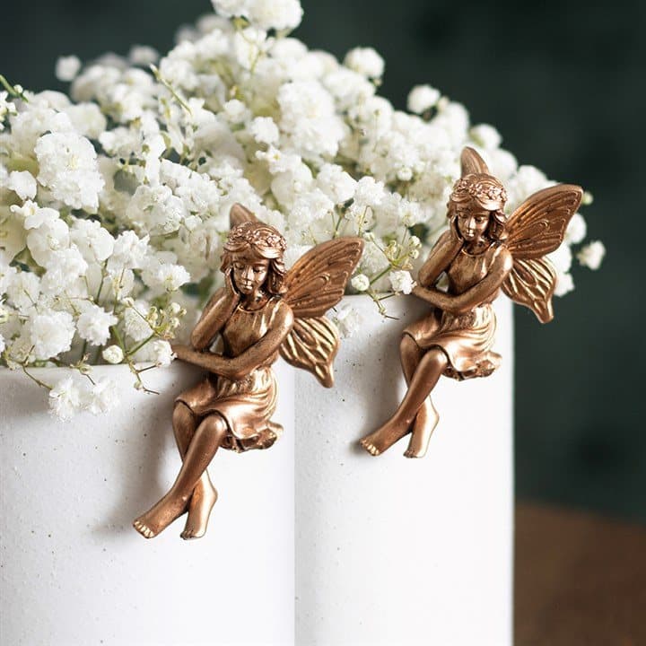 Two antique bronze effect resin fairy figures perched over a plant pot rim