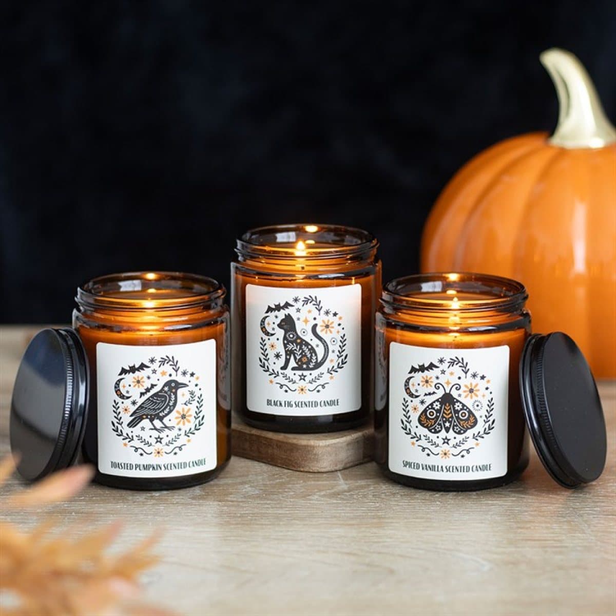 Set of three scented candles in amber apothecary-style jars with folk-inspired designs